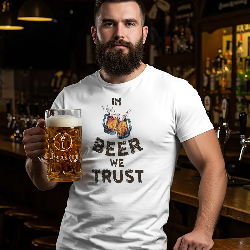 Man holding a beer mug wearing a white t-shirt with 'In Beer We Trust' text in a bar setting.