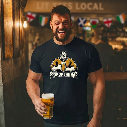 Man wearing a black t-shirt with a graphic and text saying 'Prop up the Bar', holding a beer in a bar setting.