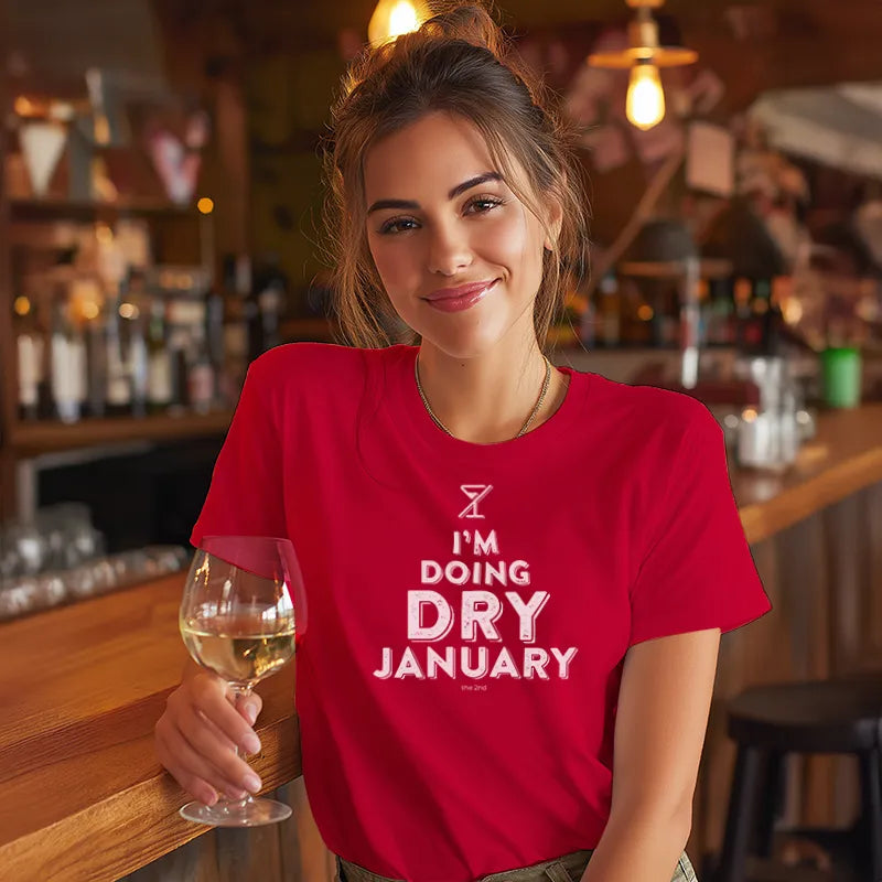 Woman in a red 'I'm Doing Dry January' shirt holding a glass of wine in a bar.