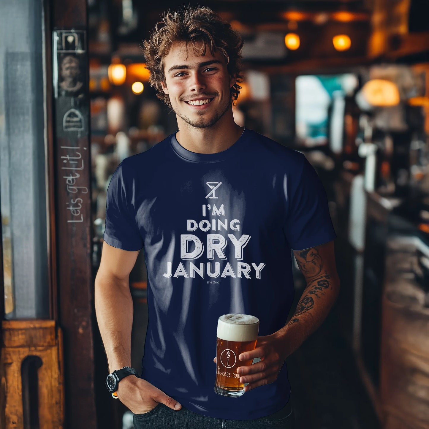 Man wearing a 'I'm Doing Dry January' t-shirt holding a beer in a bar.