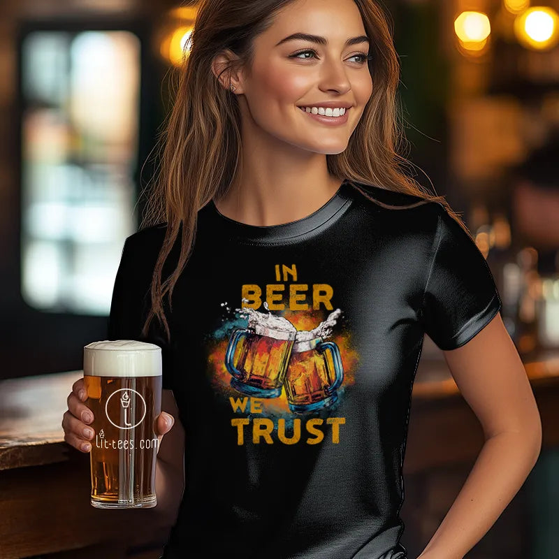 Woman wearing a black t-shirt with 'In Beer We Trust' design, holding a beer mug in a bar setting.