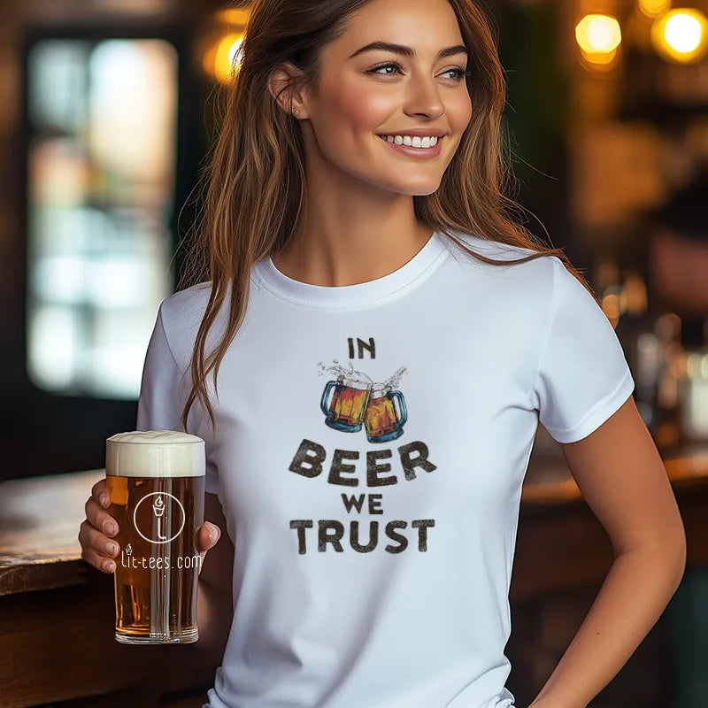 Woman wearing a 'In Beer We Trust' t-shirt holding a beer glass in a bar setting.