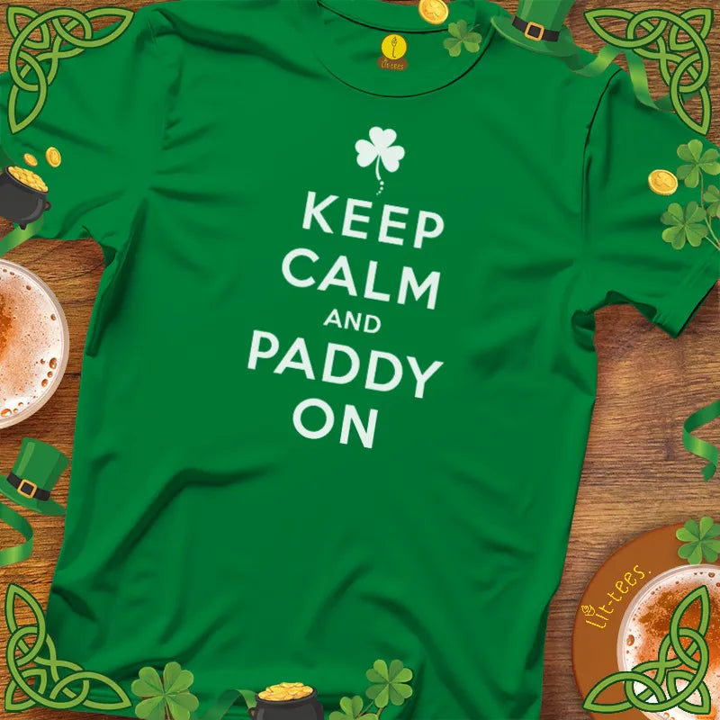 Green t-shirt with 'Keep Calm and Paddy On' text on a wooden surface with St. Patrick's Day decorations.
