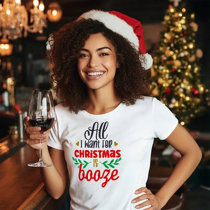 Woman wearing a Santa hat and Christmas-themed t-shirt reading 'All I want for Christmas is Booze' holding a glass of wine in a festive setting. Glass has lit-tees.com printed on it.