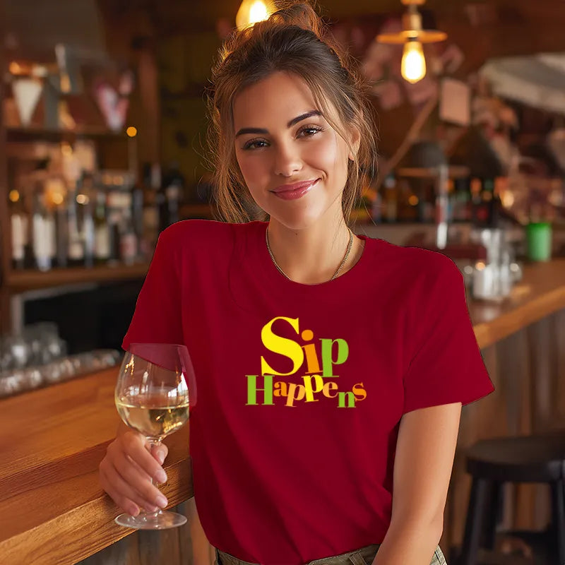 Woman in a red t-shirt with 'Sip Happens' text holding a glass of wine in a bar setting.