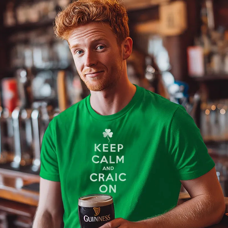 Man wearing a green t-shirt with 'Keep Calm and Craic On' holding a Guinness in a bar setting.